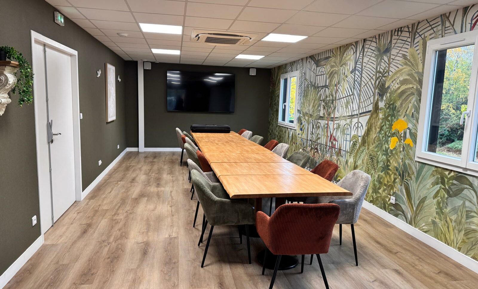 salle séminaires pour réunion professionnelle, à 10 min d'Angers (49-Maine et Loire) pouvant accueillir 20 à 40 personnes selon la configuration choisie, sur la photo, on voit les tables en bois rassemblées pour créer une grande tablée avec des fauteuils, une belle décoration et un télévision écran plat accrochée au mur.