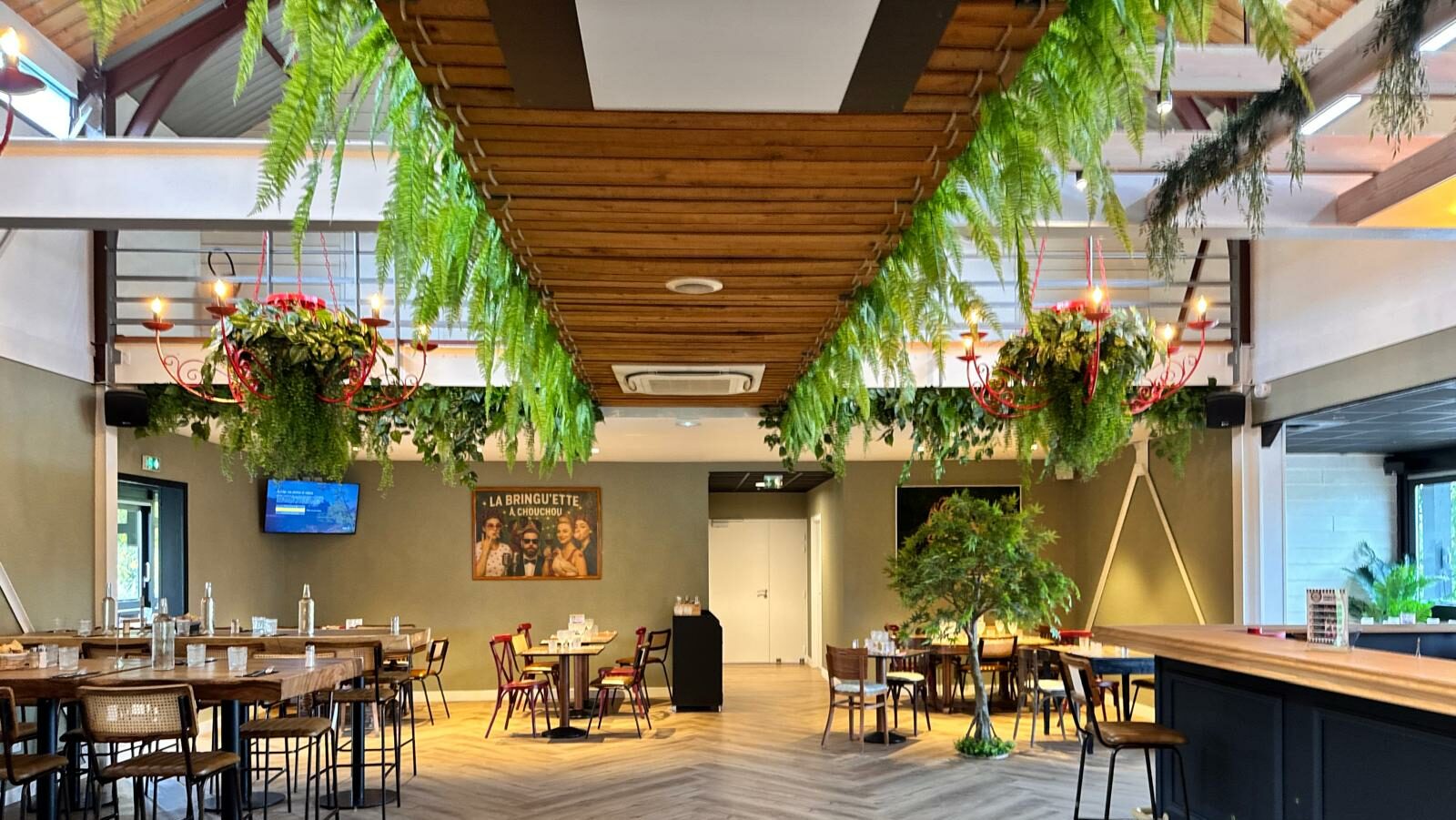 Salle principale du bar-restaurant La Bringu'ette à Chouchou, avec tables, chaises, bar et décoration végétale